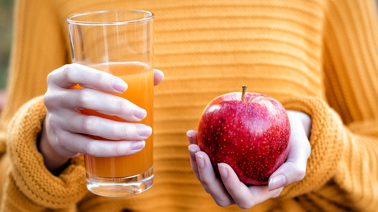 A woman in an orange sweater holding an apple and a glass of cloudy apple juice