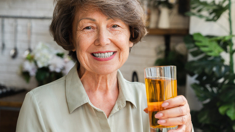 An older woman smiling as she drinks a glass of apple juice