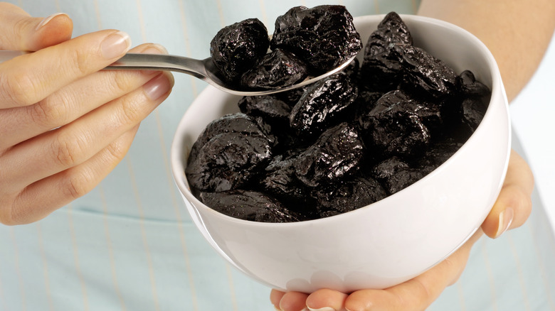 Hand scooping a spoonful of prunes out of a white bowl