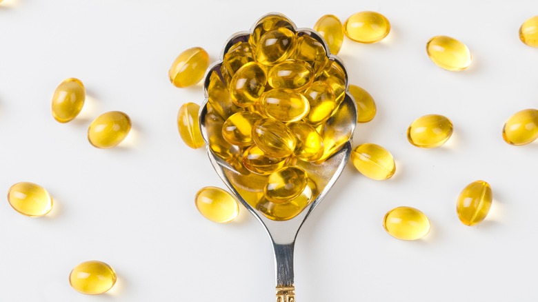 Yellow oil capsule supplements on silver spoon
