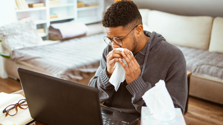 Man blowing nose at desk