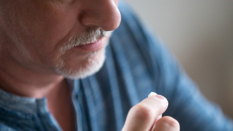 older man putting pill to his mouth