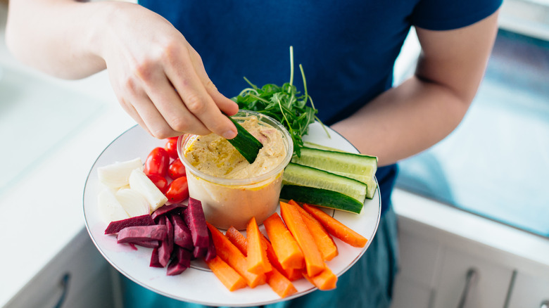 woman dipping cucumbers into hummus