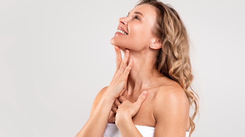 Woman in towel touching face and neck