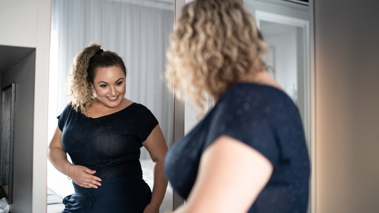 woman looking at her body while in the mirror