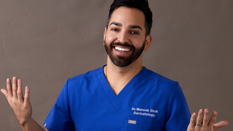 Dr. Shah in blue scrubs, smiling and shrugging