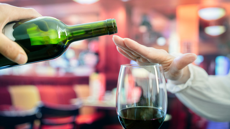 Woman's hand rejecting more alcohol from wine bottle in bar 