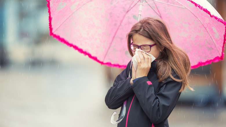 a girl blows her nose in the rain under umbrella 