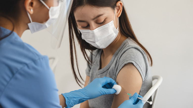 Woman with dark hair getting a shot from a doctor