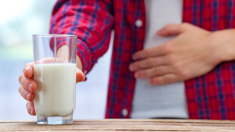 man's hand holding his stomach in front of a glass of milk