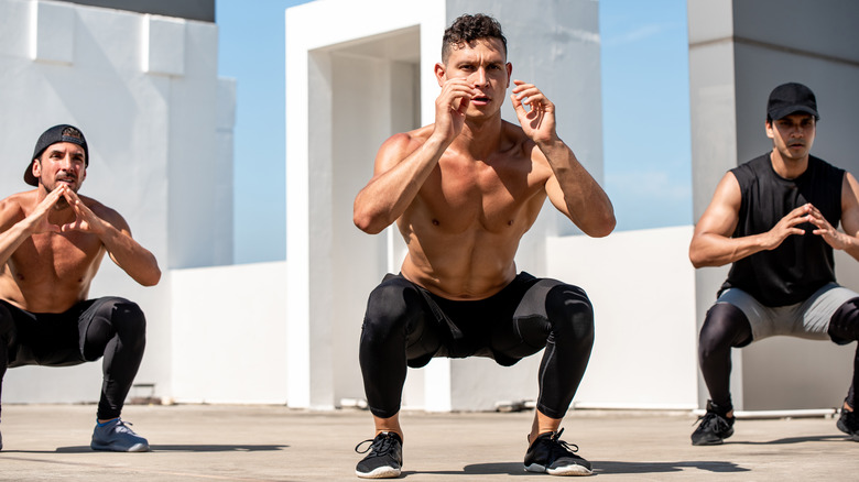 Three men sitting in squats outside