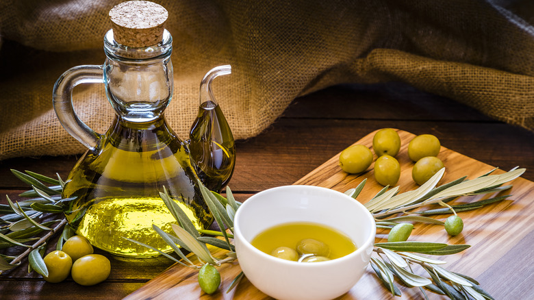 delicate bottle of olive oil surrounded by olives on a cutting board