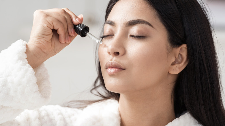 portrait of a woman with flawless skin applying drops of vitamin E oil