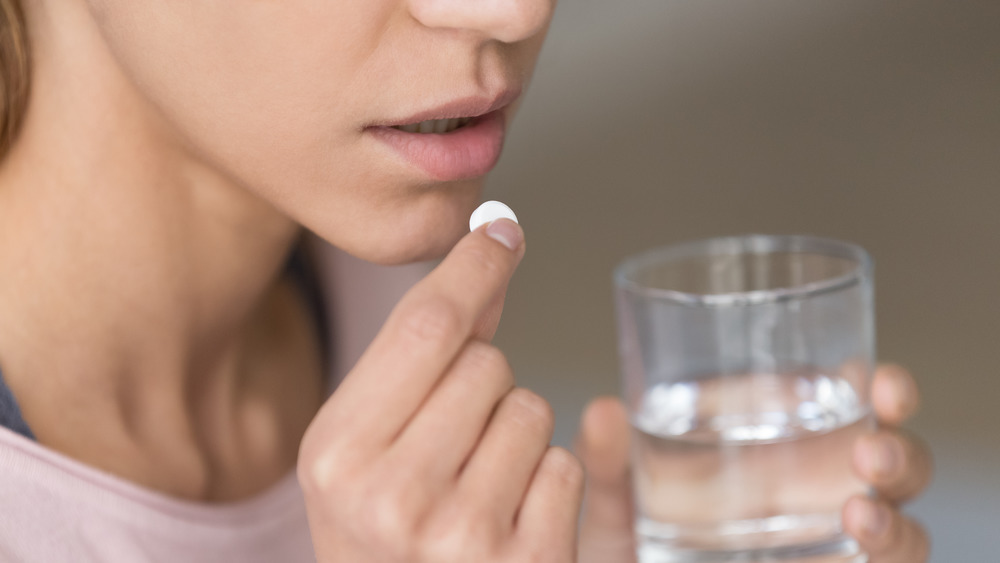 A women holding up a pill to ingest in one hand and a glass of water in the other