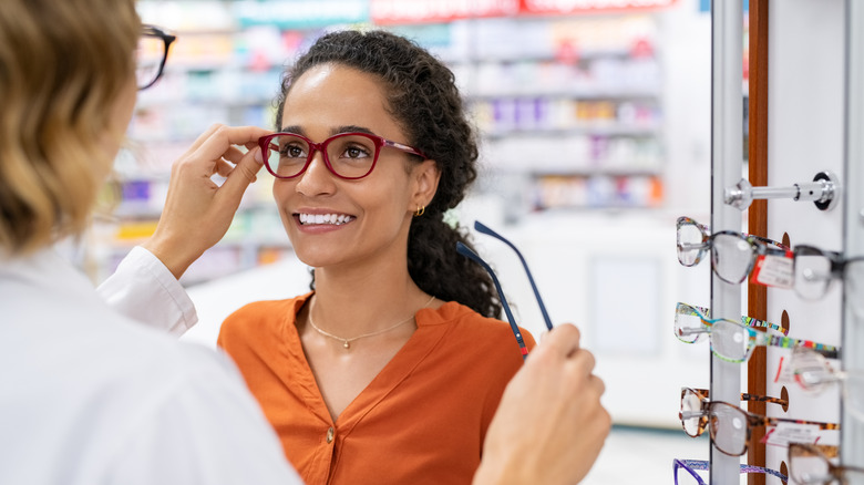 Pharmacist placing glasses on woman's face