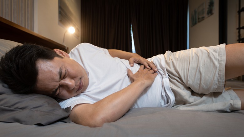 man lying on his side holding his painful abdomen