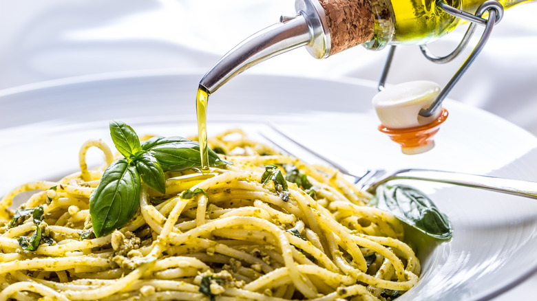 olive oil being poured onto pesto pasta