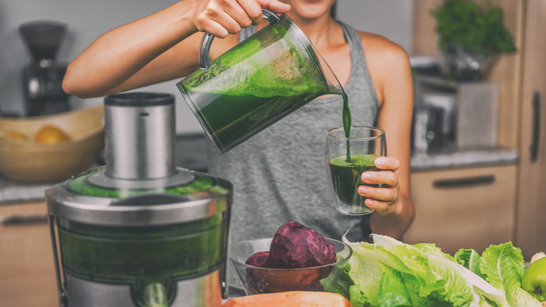 Woman is pouring green juice into a glass at home