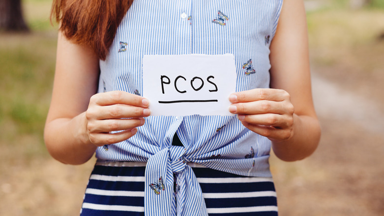 Woman holding a paper that says "PCOS"