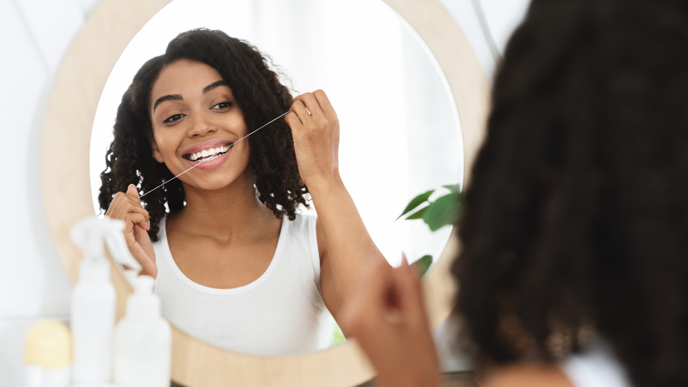 Reflection of woman flossing in the bathroom mirror