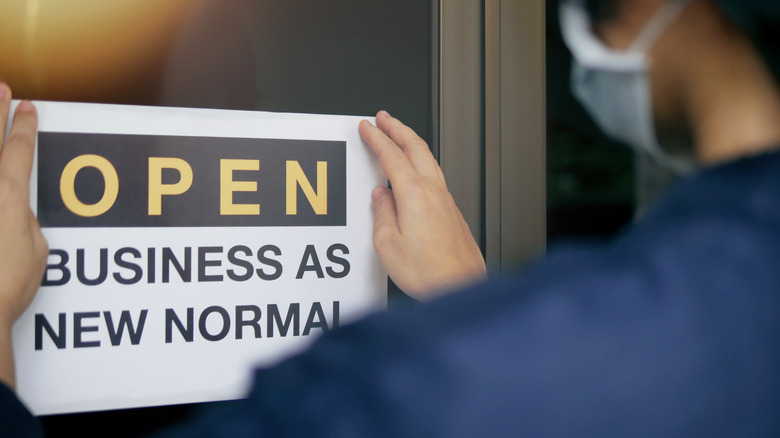 Man hanging "OPEN BUSINESS AS NEW NORMAL" sign on glass door