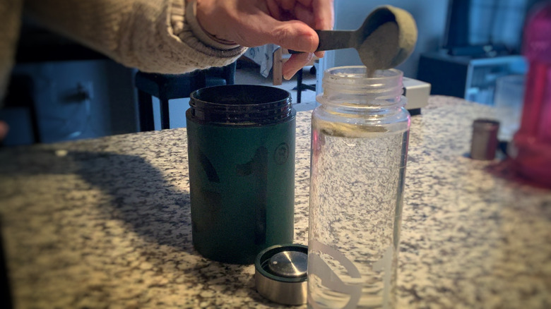 A scoop of greens powder emptying into a bottle