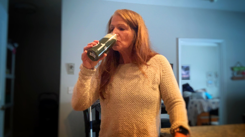 A woman drinking a green drink in the kitchen