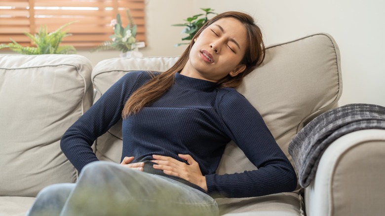 Woman on couch, having stomach pain 