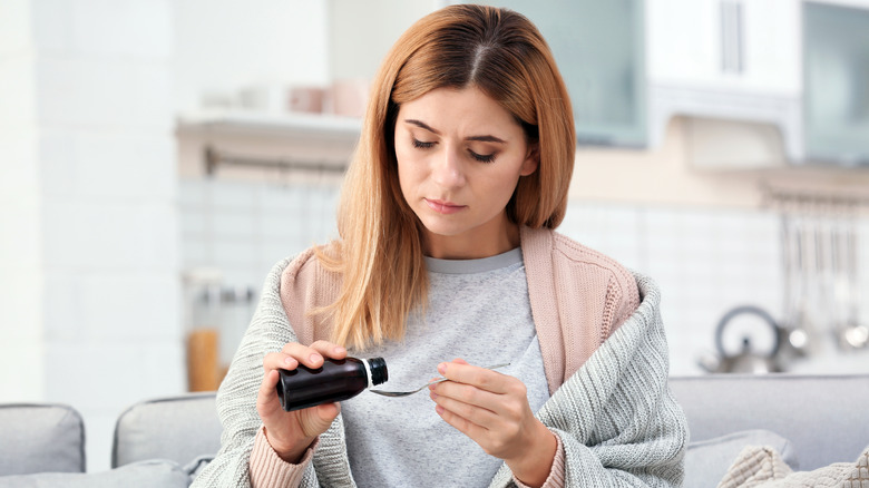 Pair of hands holding a cough syrup bottle against a drug store shelf