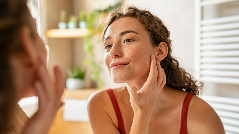 A woman looks at her face in the mirror