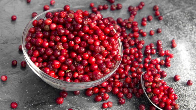 A glass bowl of cranberries spilling out on a table