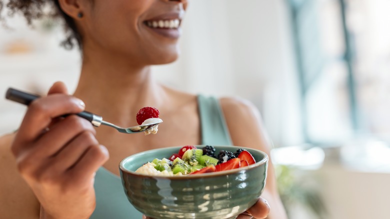 A woman holding a bowl of healthy fruits, vegetables, and whole grains