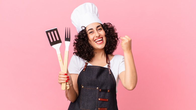 a woman smiling holding grill tools 