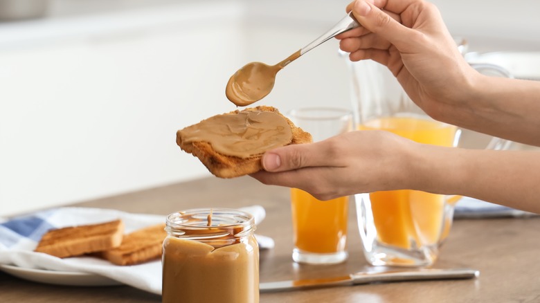 woman's hands spooning peanut butter on bread