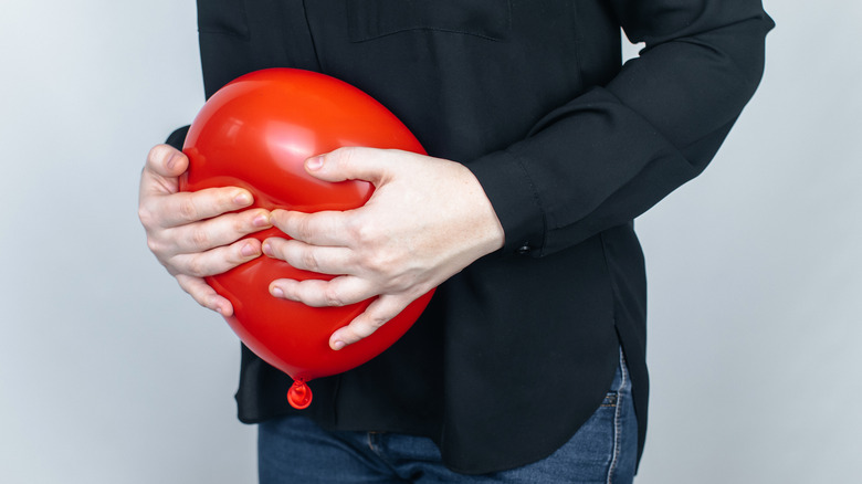 Hands holding a red balloon up against their stomach