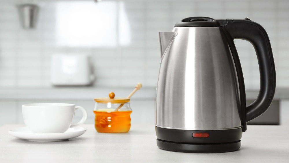 An electric kettle a tea cup and a small jar of honey on a kitchen counter