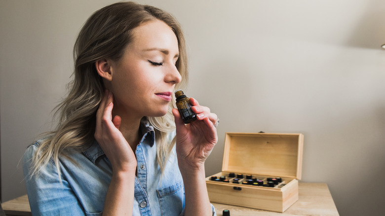 Woman sitting at desk inhaling an essential oil vial next to an open wooden box of other essential oils