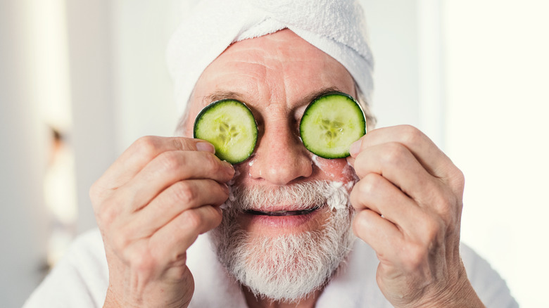 senior man holding cucumbers to his eyes 