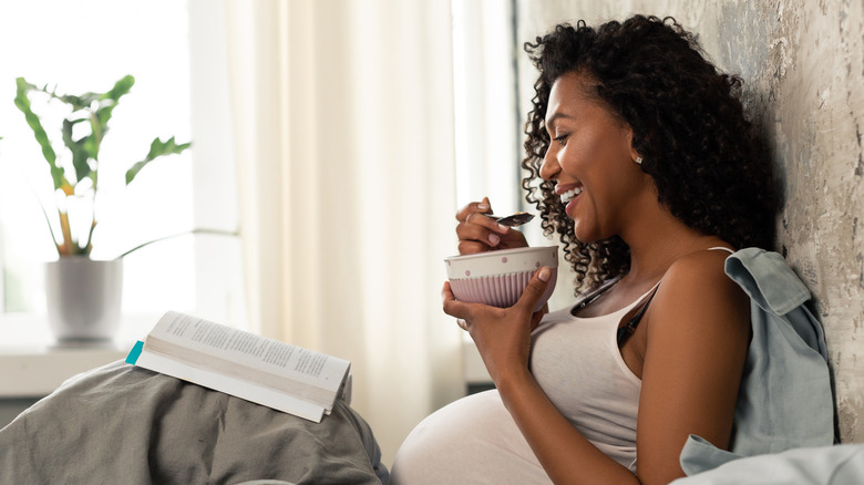 Smiling pregnant woman eating in bed