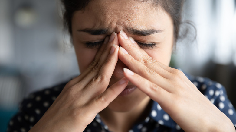 Grimacing woman pressing fingers to nose  