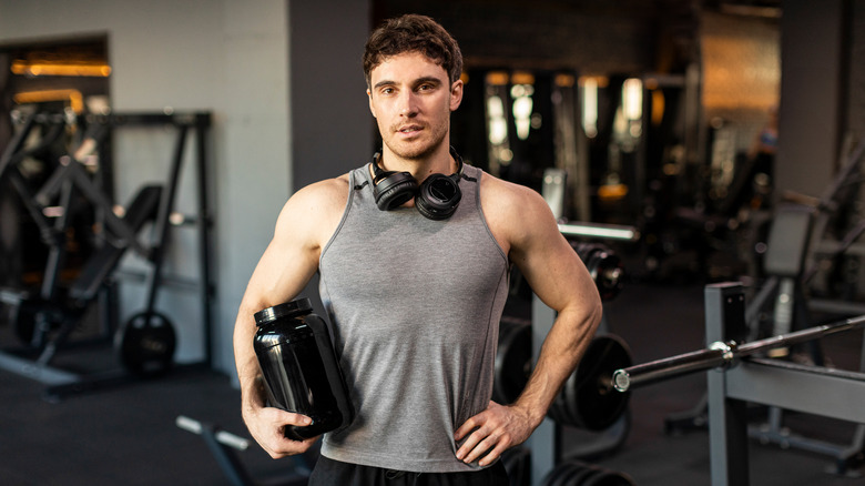 man in weight room holding a tub of supplement powder