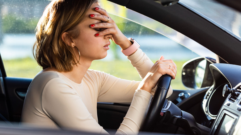 Women holding forehead while sitting in driver's seat