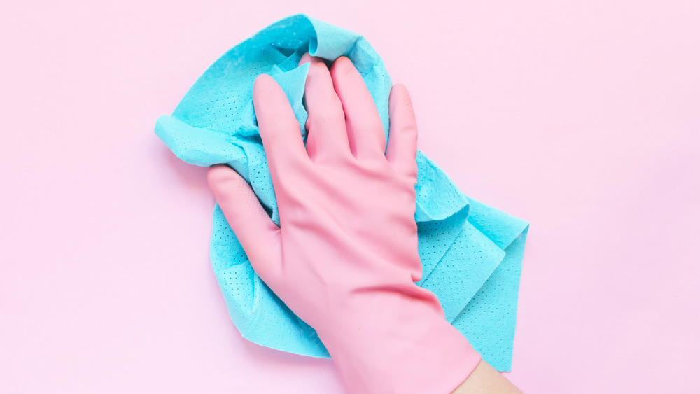 A protective rubber glove between a hand and cleaning wipe with a pink background 