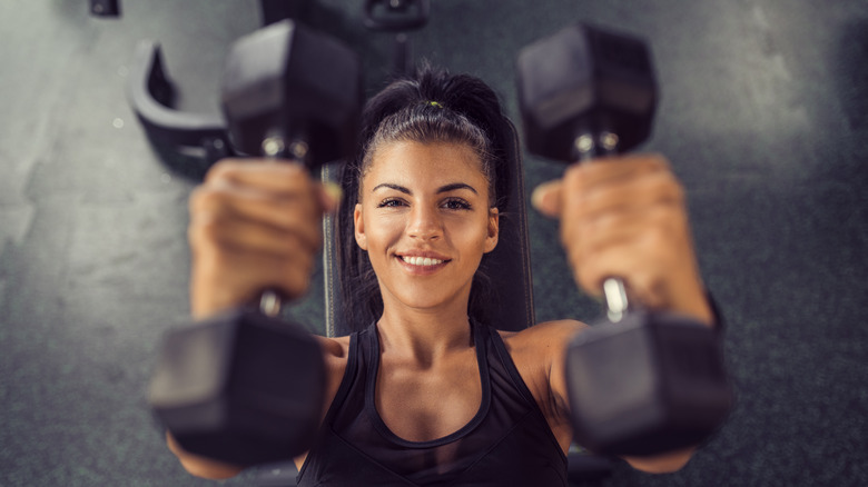 ﻿Top view of smiling woman lifting dumbbells in gym