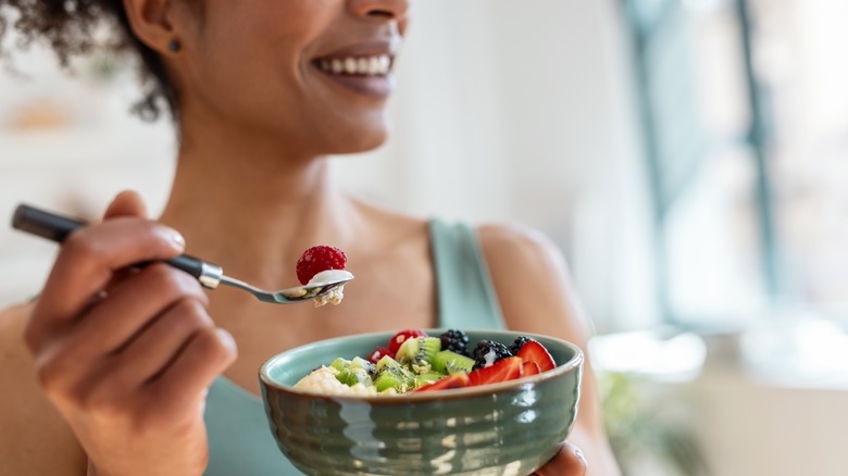 A woman eating a bowl of fruit and vegetables