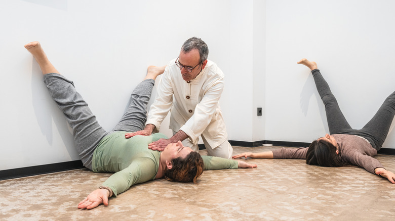 A yoga instructor helping a woman whose legs are in a straddle on a wall