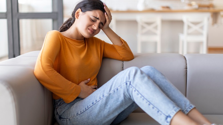 woman on couch holding stomach and head in pain