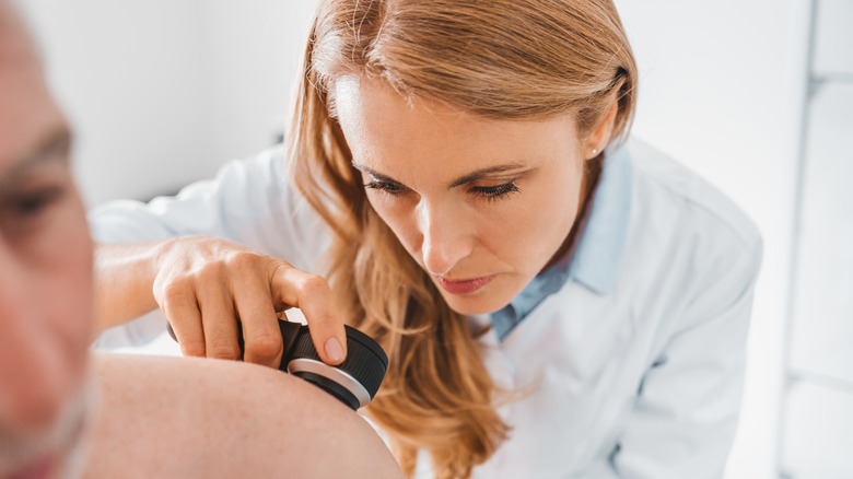 Doctor uses a magnifying glass to examine a patient's skin 