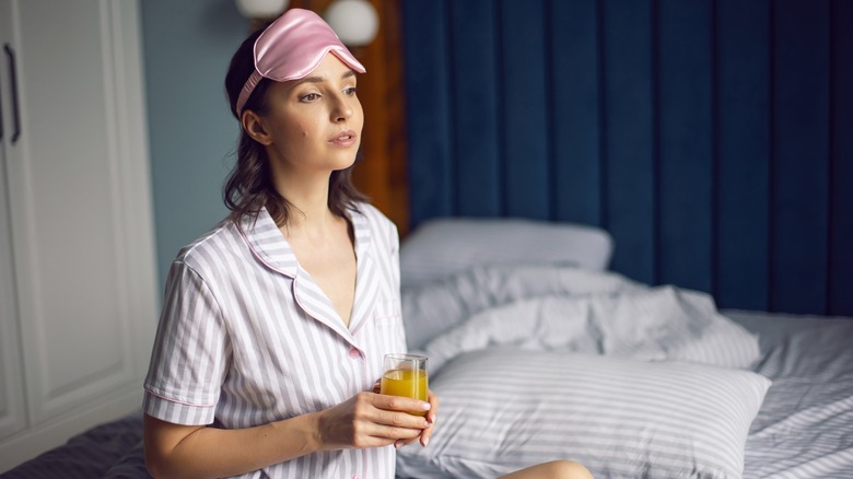 young woman holding juice while in bed