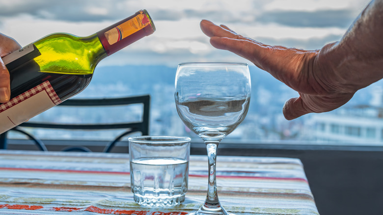 A man's hand halting the pouring of more wine into his glass